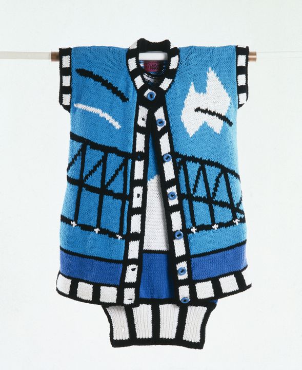 The knitted coat is part of a women's ensemble designed by Jenny Kee and made by Jan Ayres for Flamingo Park. The cardigan-style coat has short sleeves, a round neck, a front buttoning closure and a ribbed band at the bottom. The Sydney Harbour Bridge is depicted in black across the centre front. A stylised white Australia shape, crossed by a black diagonal line, lies on the right breast. Two parallel, diagonal lines, one black, one white, lie on the left breast. A band of blue runs beneath the Bridge representing the sea. 